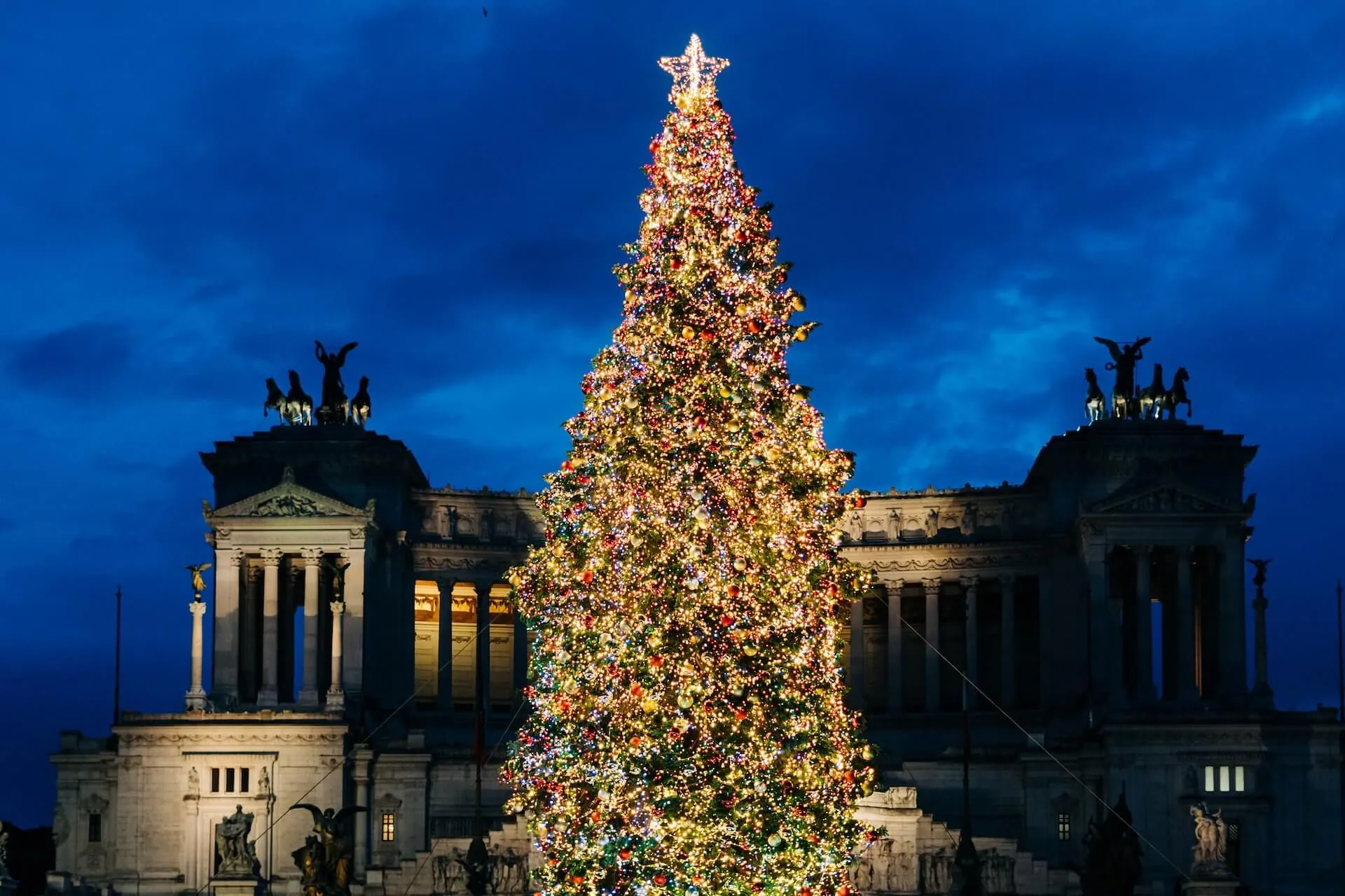 Large illuminated Christmas tree standing in front of the Altar of the Fatherland (Altare della Patria) monument in Piazza Venezia, Rome, at night