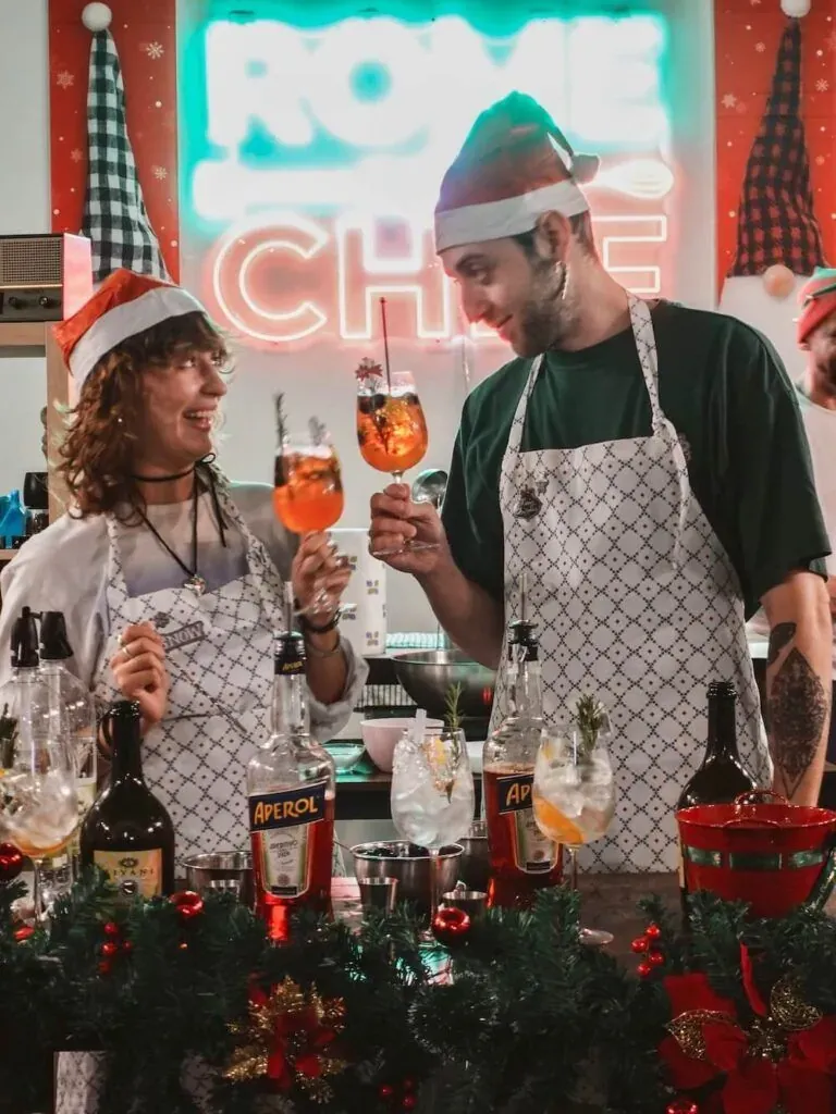Couple wearing Santa hats toasting with drinks during a festive Christmas cooking class