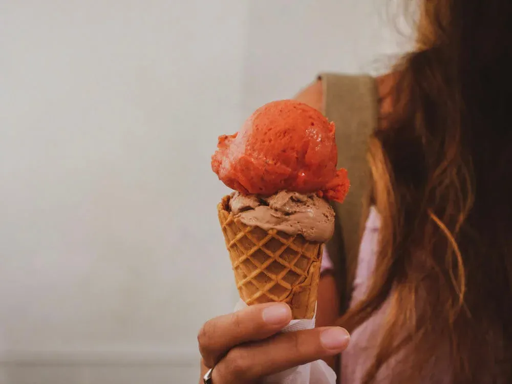 Young woman holding up a cone of chocolate and strawberry gelato in Rome