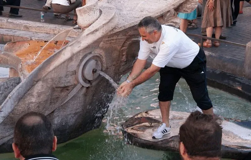 Man filling water bottle at the Fontana della Barcaccia (Fountain of the Old Boat) in Rome