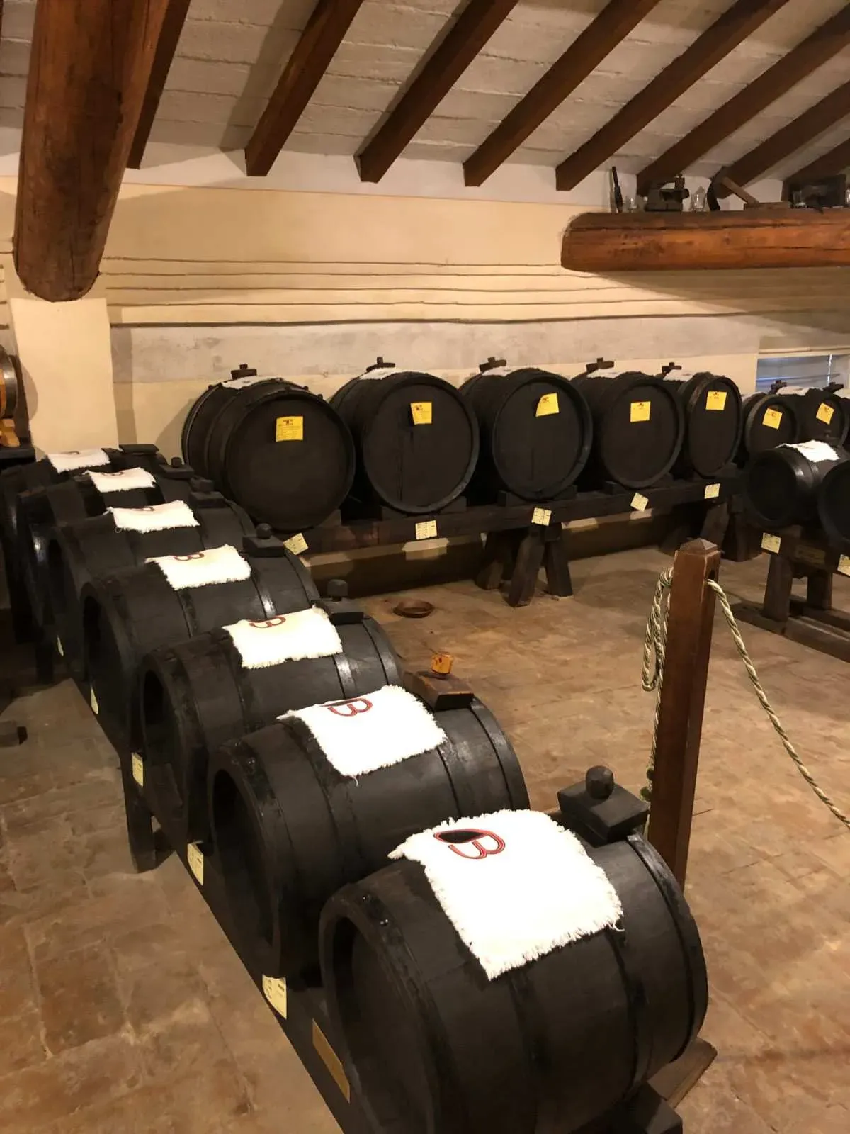 Rows of traditional balsamic vinegar aging barrels with white cloth labels and yellow identification tags, demonstrating the meticulous labeling and tracking system used in authentic balsamic vinegar production.