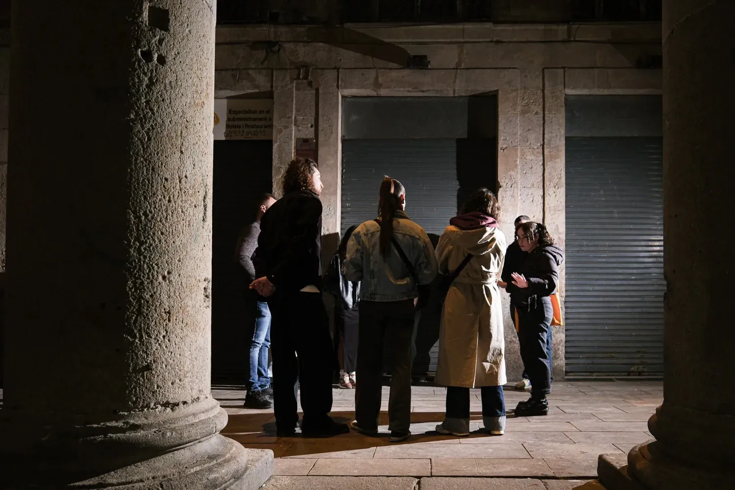 A group of ghost tour participants gathered near the massive Gothic columns of Basilica de Santa Maria del Pi, with dramatic stone architecture and shadows creating an eerie atmosphere.
