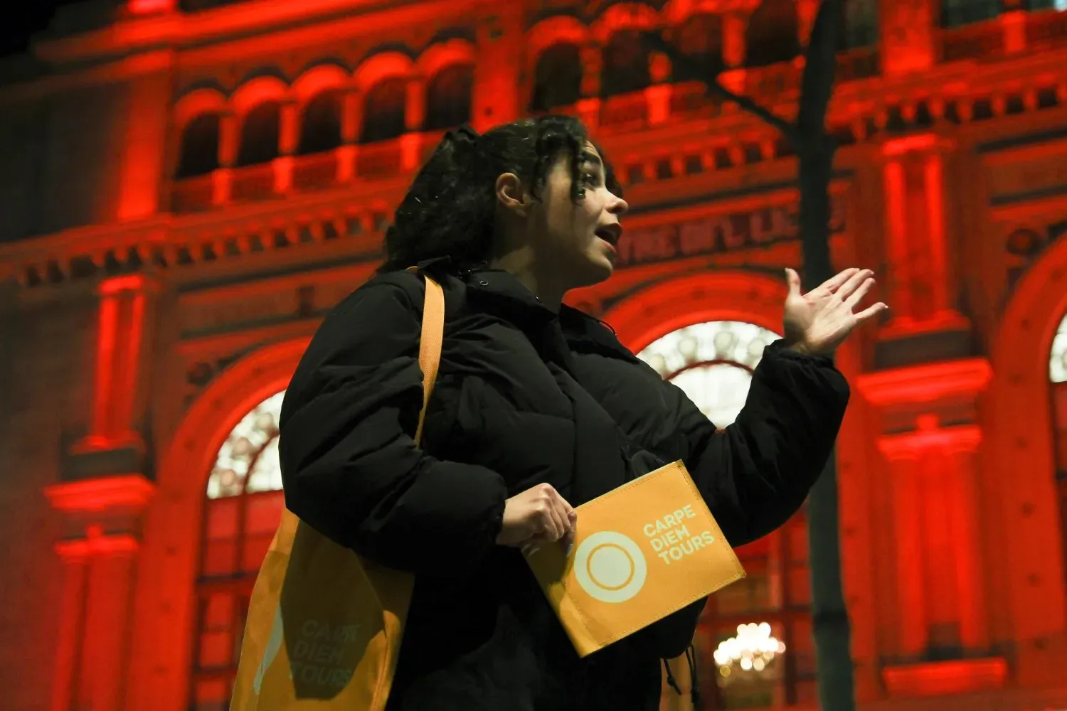 A Carpe-Diem Tours guide passionately telling ghost stories in front of the red-lit Liceu Opera House in Barcelona, sharing tales of the building's haunted history and dark past.