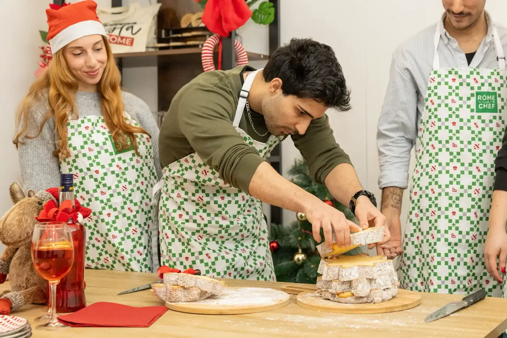 Close-up of hands garnishing orange cocktails with fresh rosemary and blueberries next to a decorative dessert tower during a culinary class