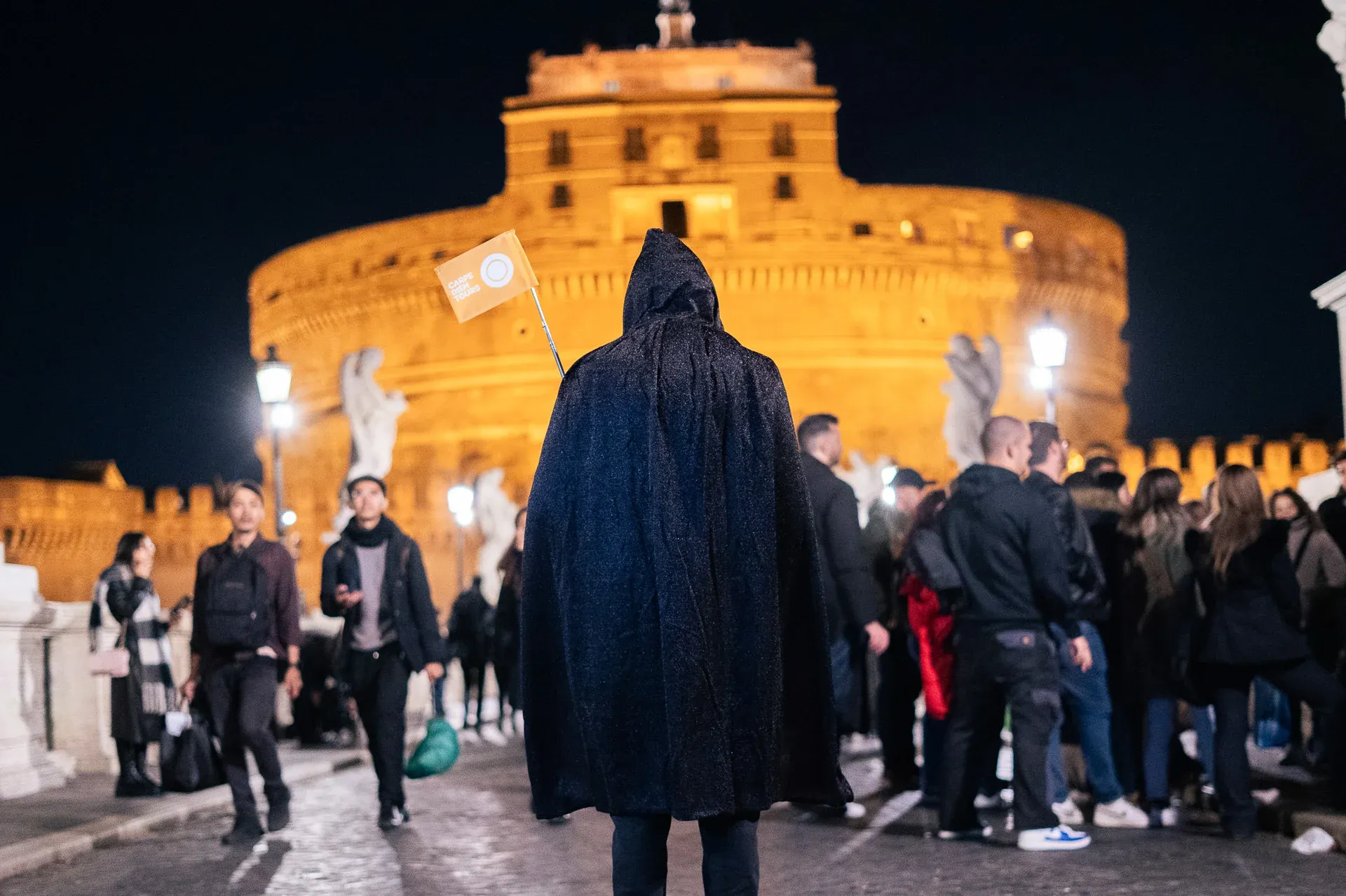 A mysterious guide in a dark cloak standing before the Castel Sant'Angelo on a Rome ghost tour.
