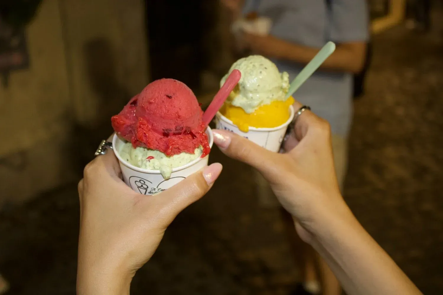 Two hands holding artisan gelato cones with vibrant flavors including strawberry, pistachio, and lemon, representing the final sweet course of the Rome food tour.