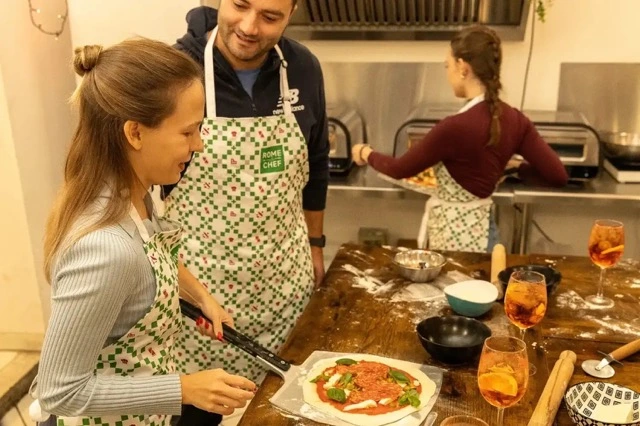 Student enjoying Aperol Spritz cocktail while preparing homemade pizza in Rome cooking class kitchen