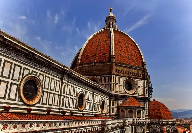 Florence Duomo Cathedral with iconic red terracotta dome, white and green marble inlay, and golden cross against blue sky