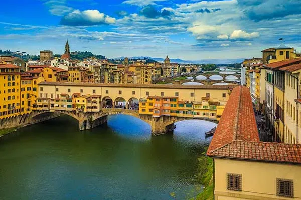 Iconic Ponte Vecchio bridge with historic buildings and shops spanning the Arno River in Florence with blue water reflection
