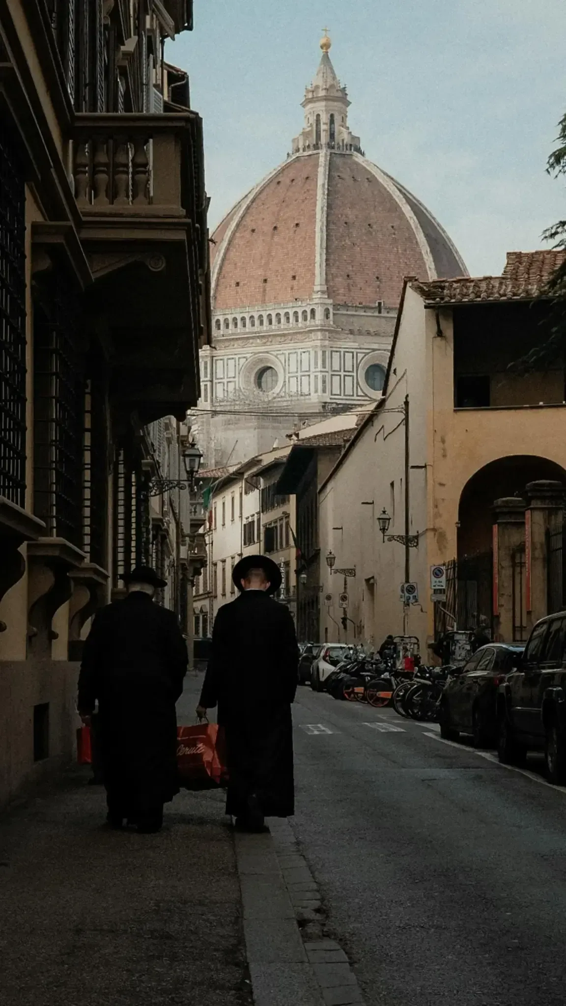 Pedestrians walking on historic Florence street with view of Brunelleschi dome and traditional Renaissance buildings