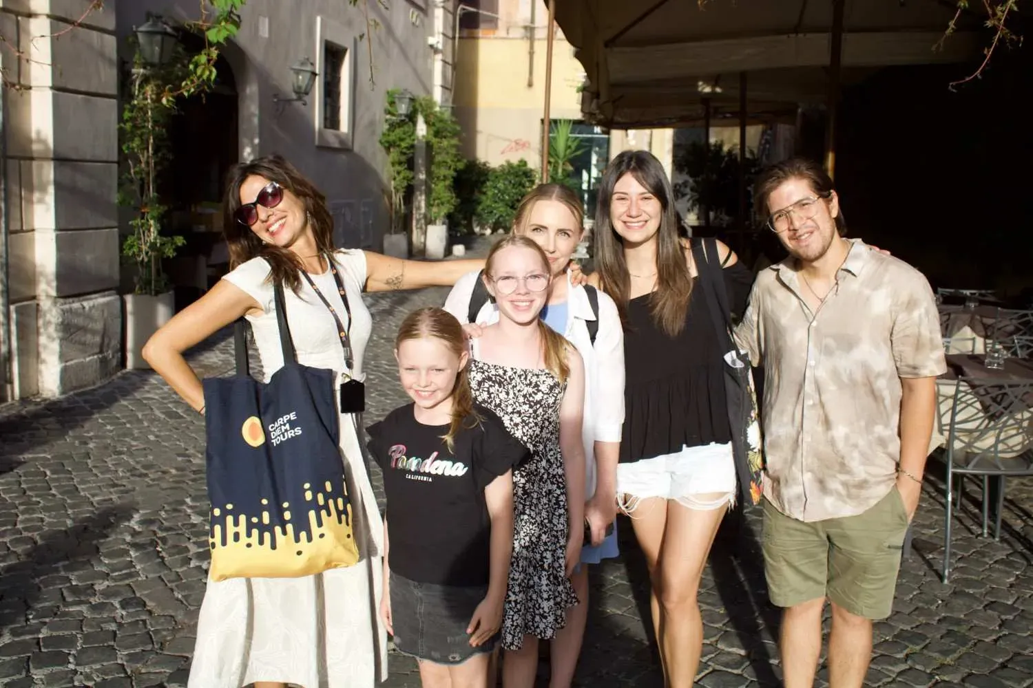 A happy group of six food tour participants posing together on a charming cobblestone street in the Trastevere neighborhood of Rome.