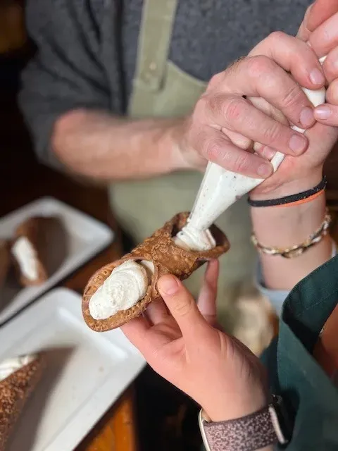 A close-up of hands piping fresh ricotta cheese into a crispy pastry shell during a traditional Tuscan cooking class experience.