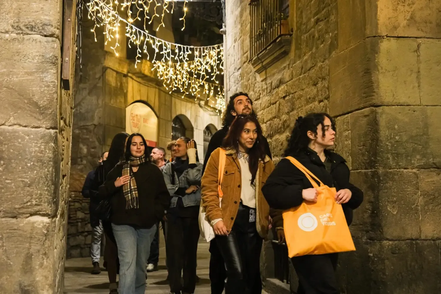 A group of ghost tour participants gathered in a narrow stone alley in El Born with dramatic stone architecture and atmospheric lighting, exploring the haunted history of Barcelona.