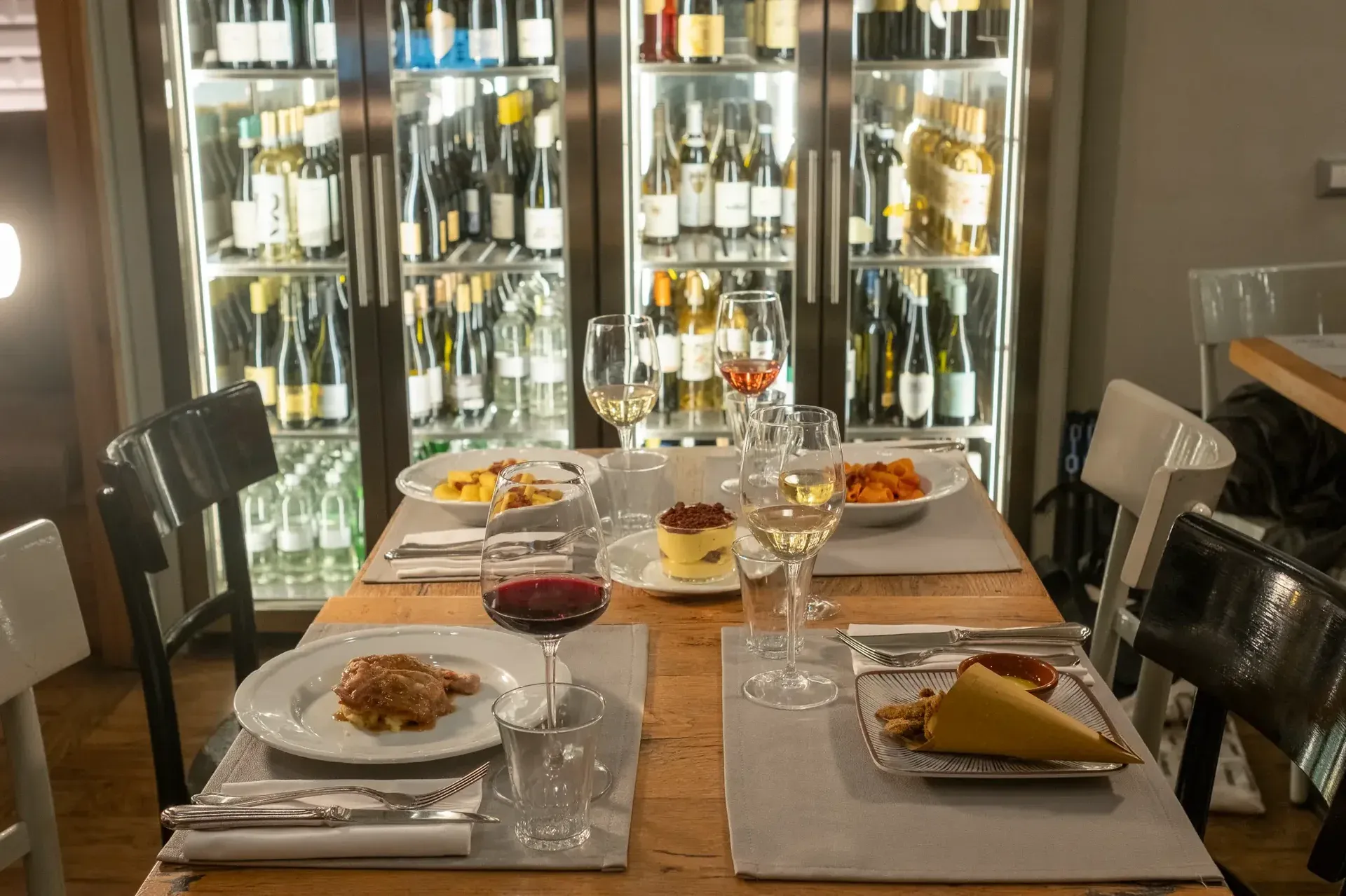 A beautifully set gourmet table for two with a wine cellar in the background.