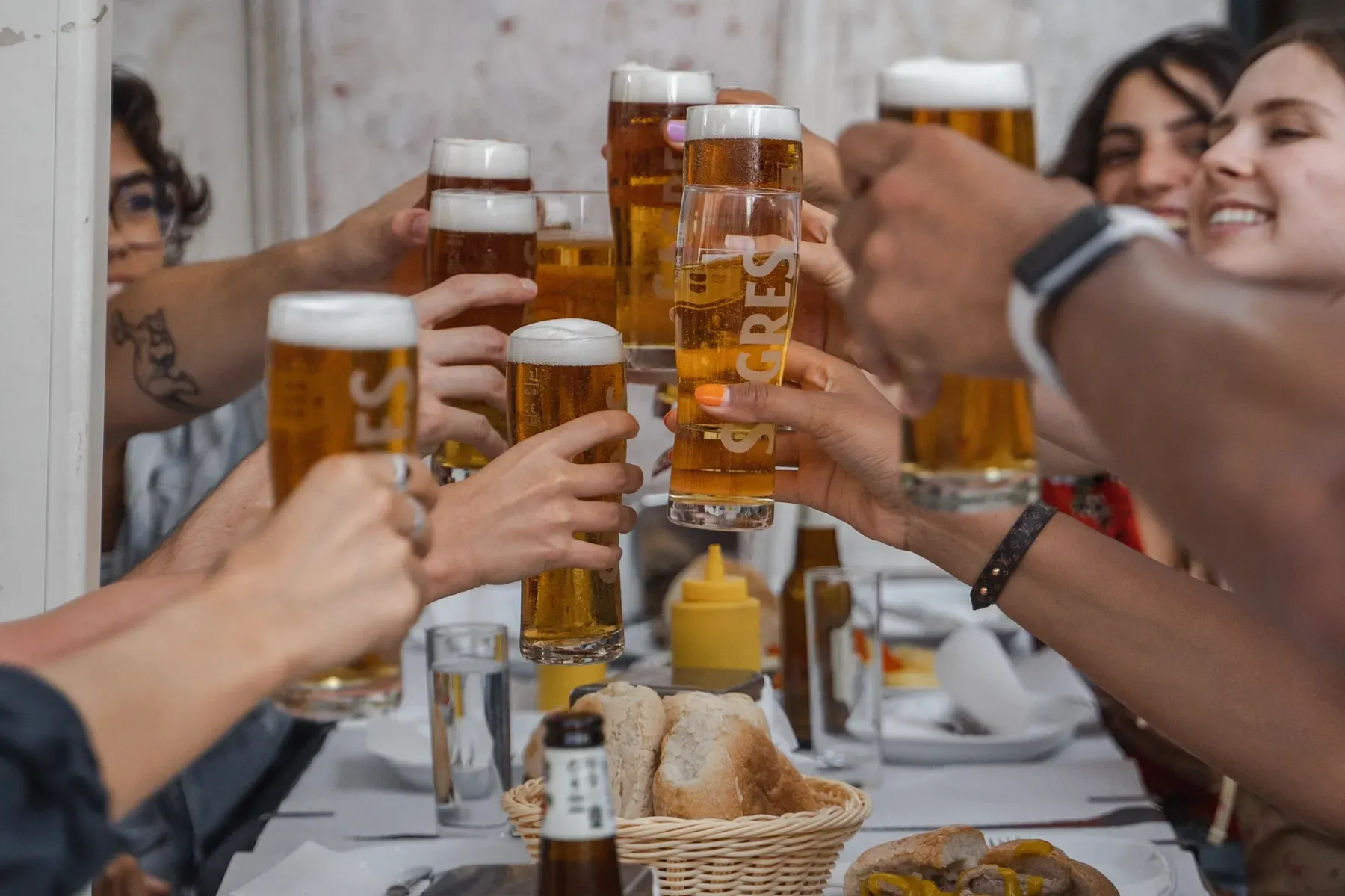 Happy group of friends toasting with tall glasses of Sagres beer and foam at a restaurant table with bread and food.