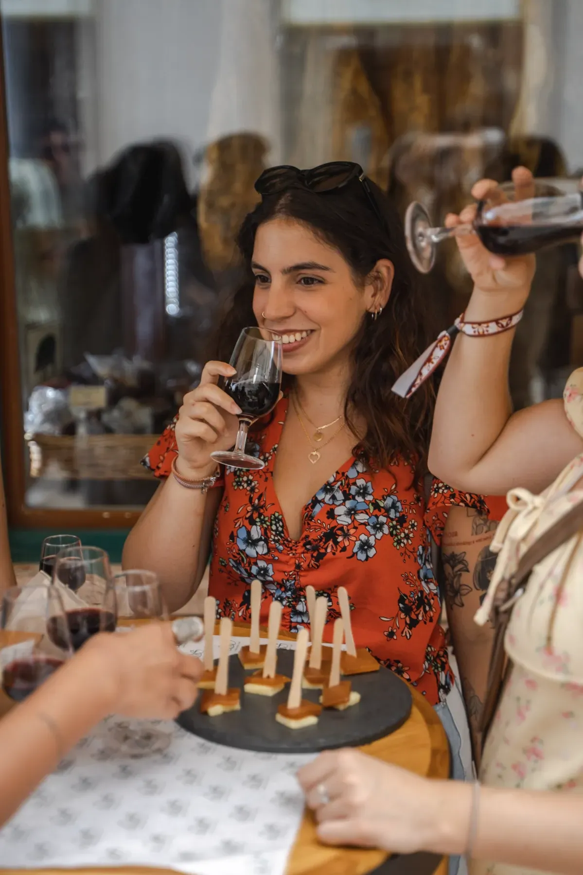 Joyful woman on a Lisbon tipsy tour, smiling while sipping red wine and sampling Portuguese cheese and quince paste tapas.