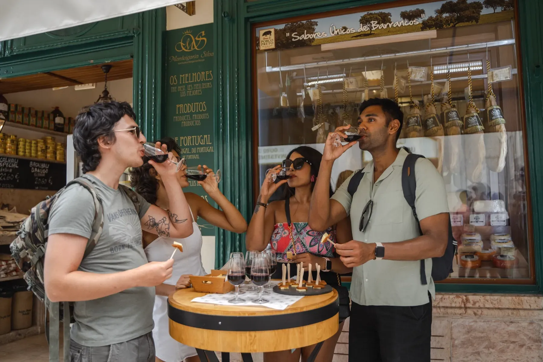 Three tourists enjoying a red wine and charcuterie tasting outside a traditional Portuguese shop in Lisbon.
