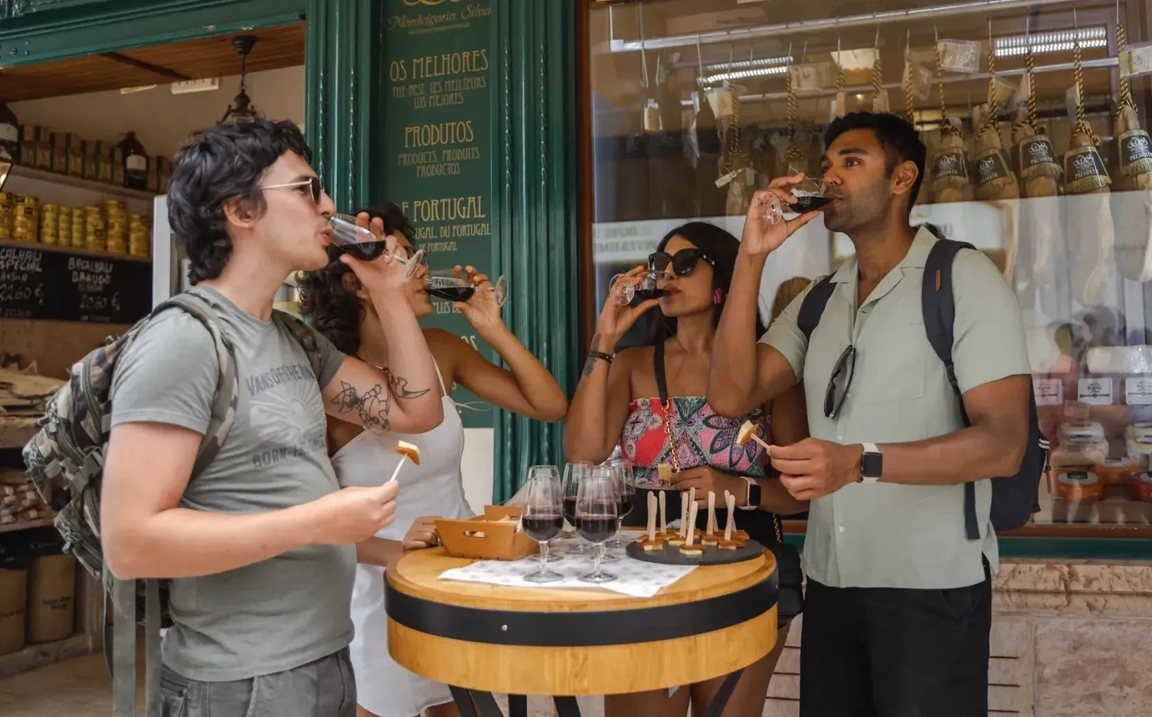 Three tourists enjoying a red wine and charcuterie tasting outside a traditional Portuguese shop in Lisbon.
