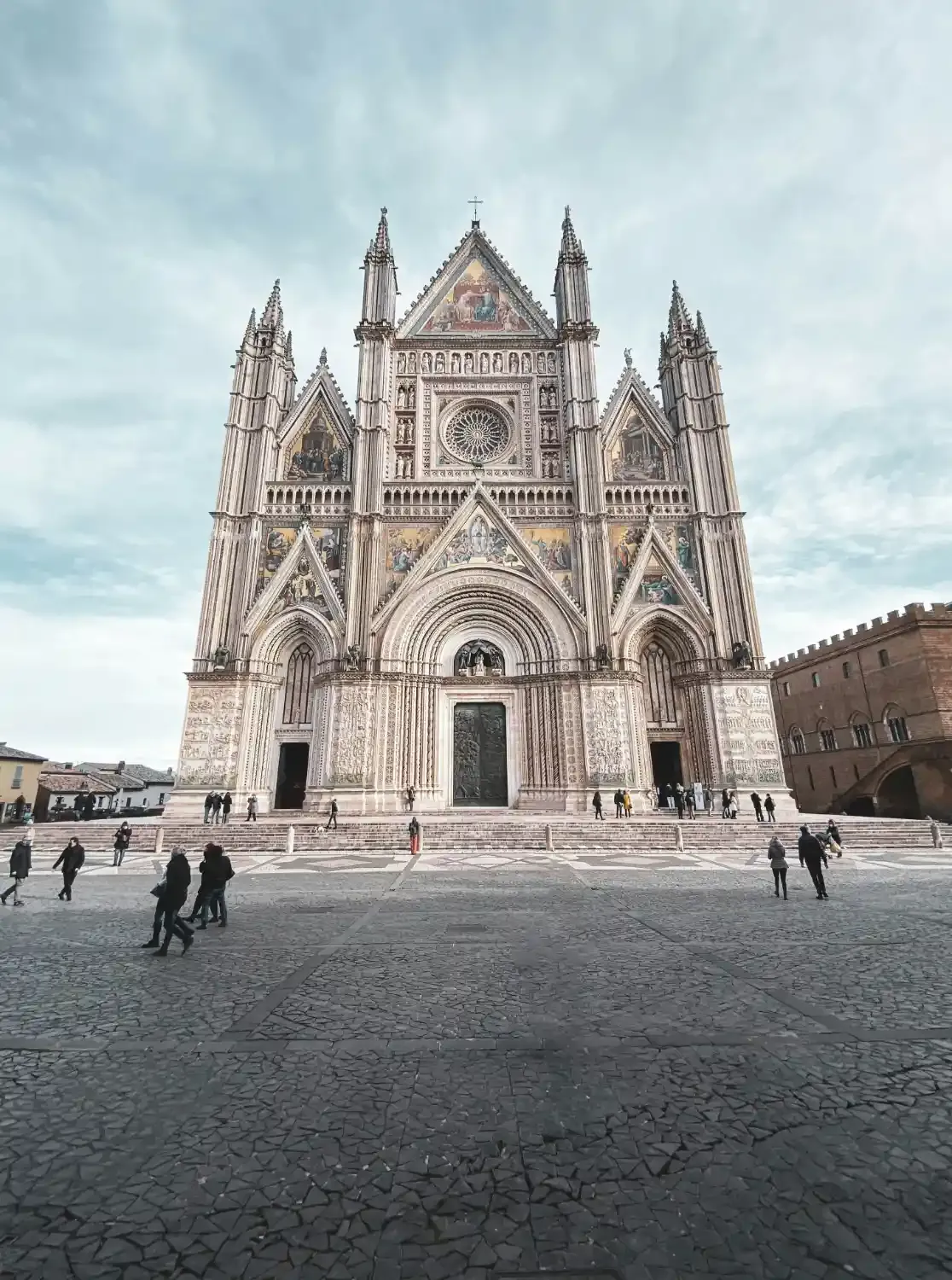 Orvieto Cathedral in main piazza with tourists Gothic spires and ornate white marble architectural details