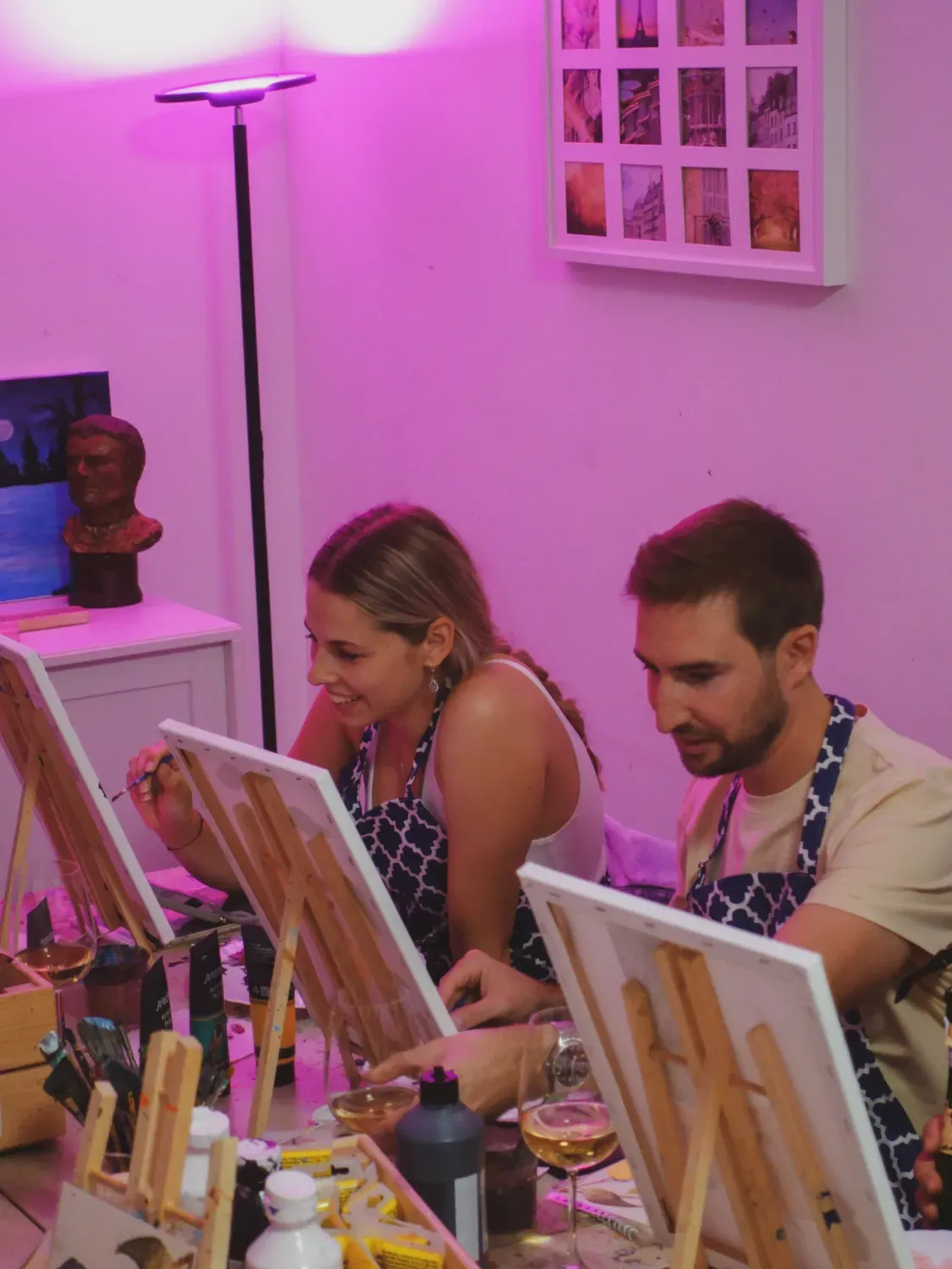 Group of participants painting with wine glasses under vibrant pink neon lighting in modern art studio