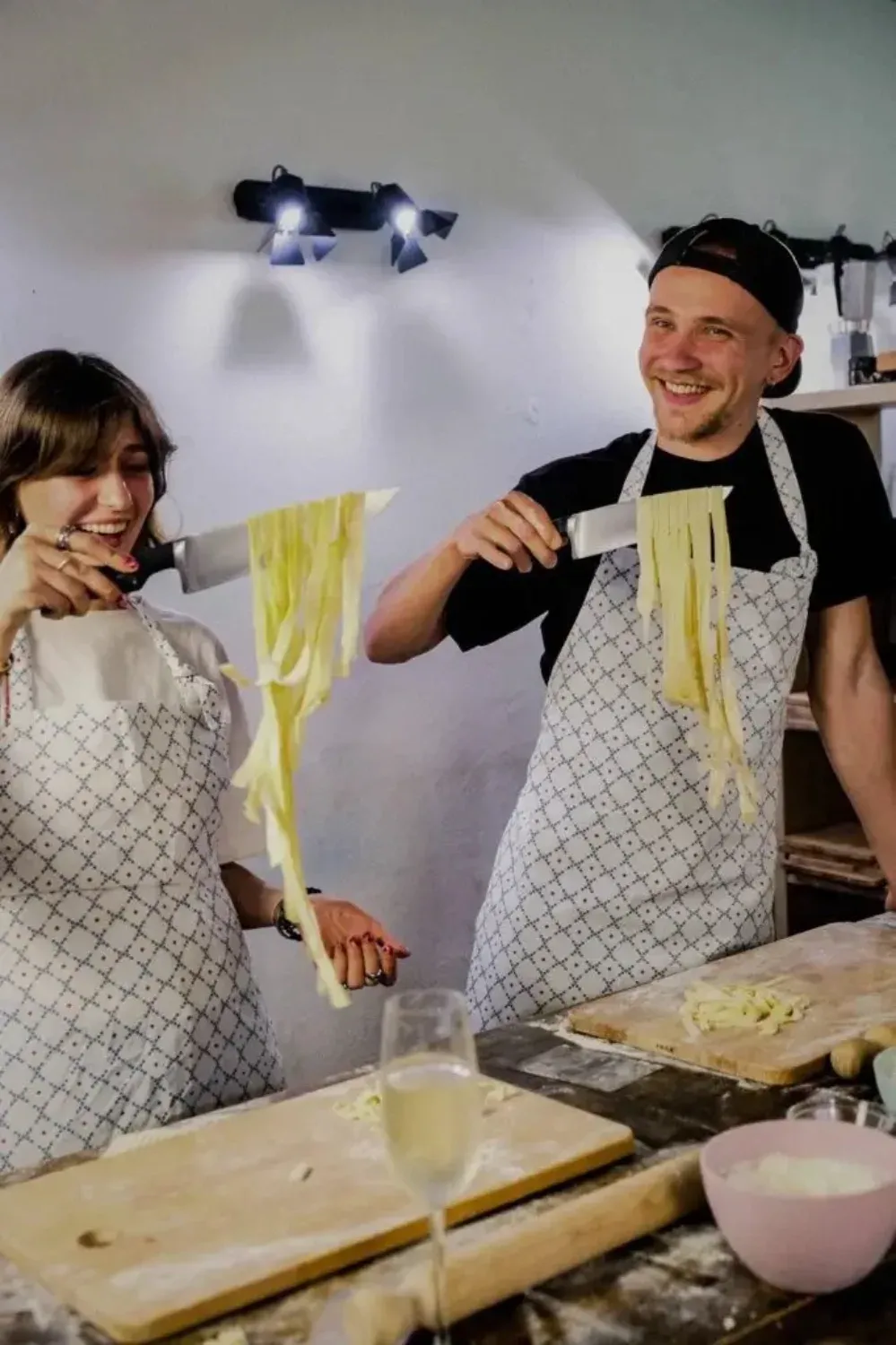 Happy couple in Rome with Chef aprons laughing while holding fresh homemade pasta strands they made during the cooking class