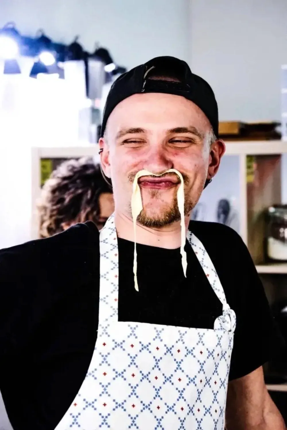 Man in Rome with Chef apron playfully holding fresh pasta strands in his mouth with a big smile during the cooking class