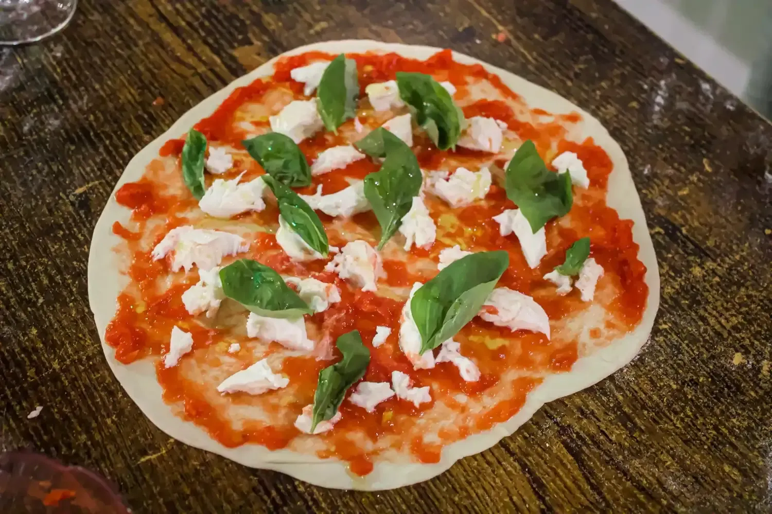 Close-up of a freshly made Margherita pizza with red tomato sauce, white mozzarella, and fresh green basil leaves