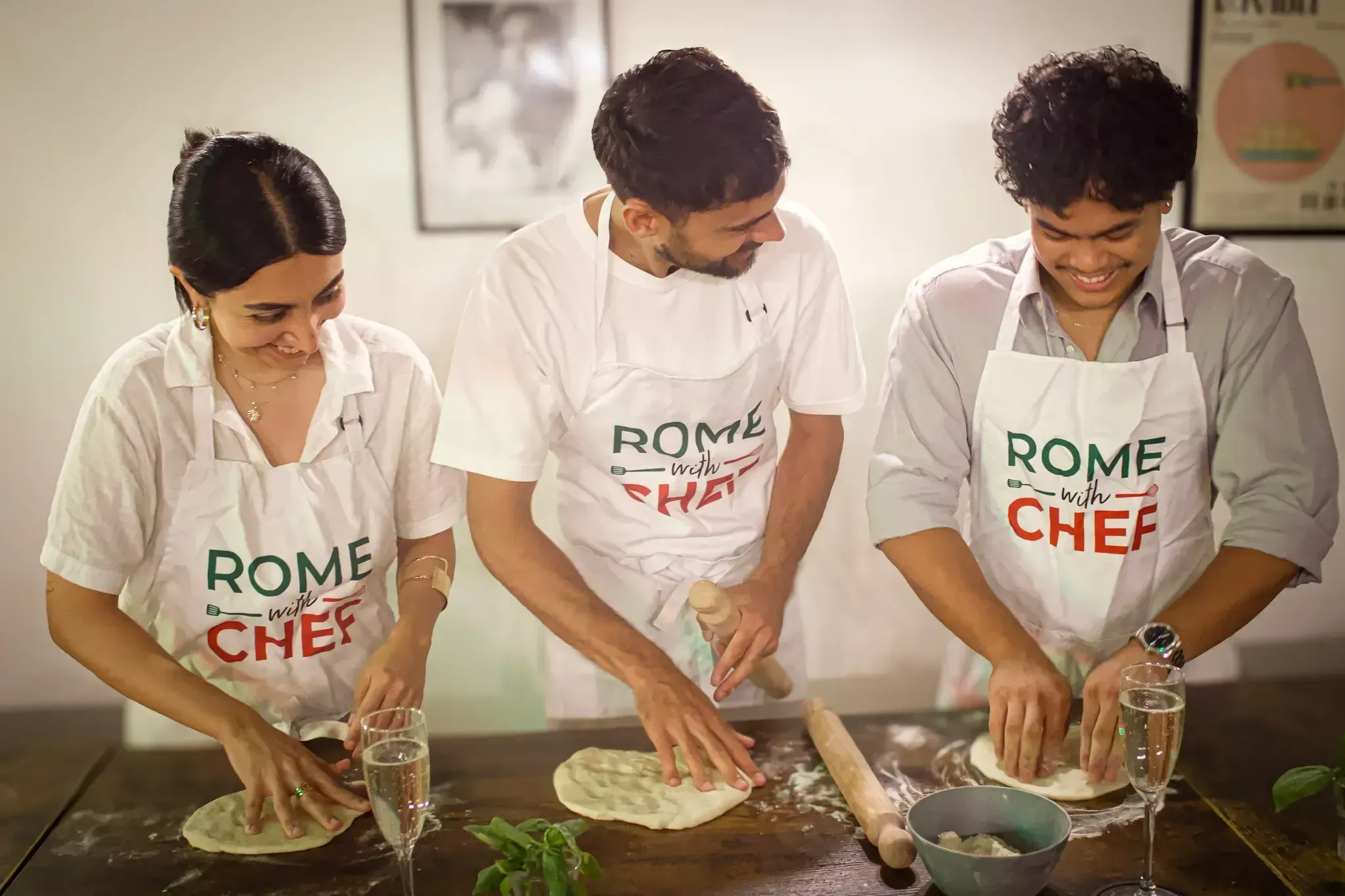 Three participants in Rome with Chef aprons kneading and stretching pizza dough on a dark table