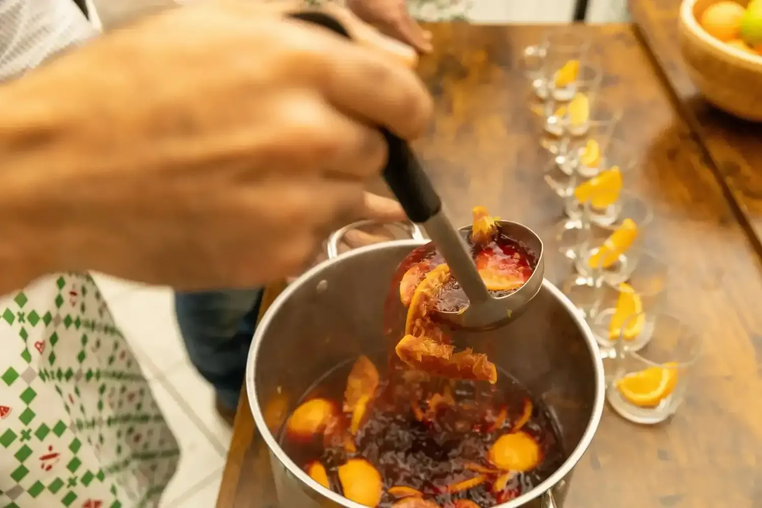 Chef using a spoon to caramelize orange slices in a pot of mulled wine with sugar and spices