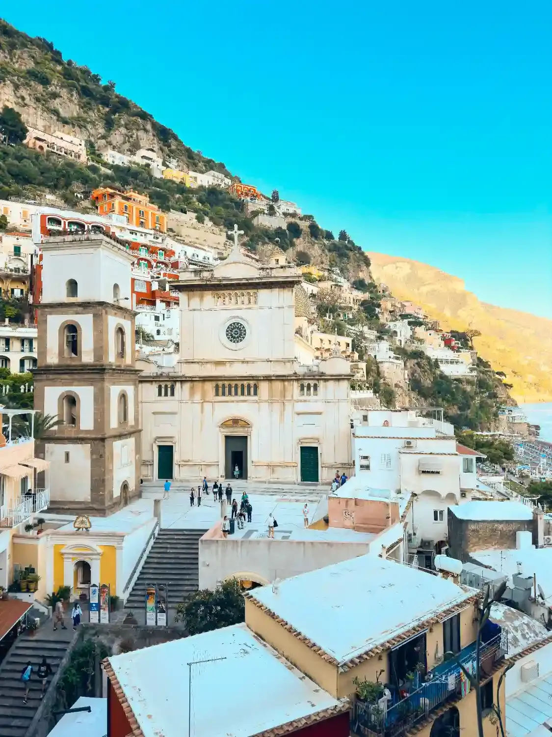 Historic church with distinctive bell tower in Positano overlooking colorful village buildings and Mediterranean Sea