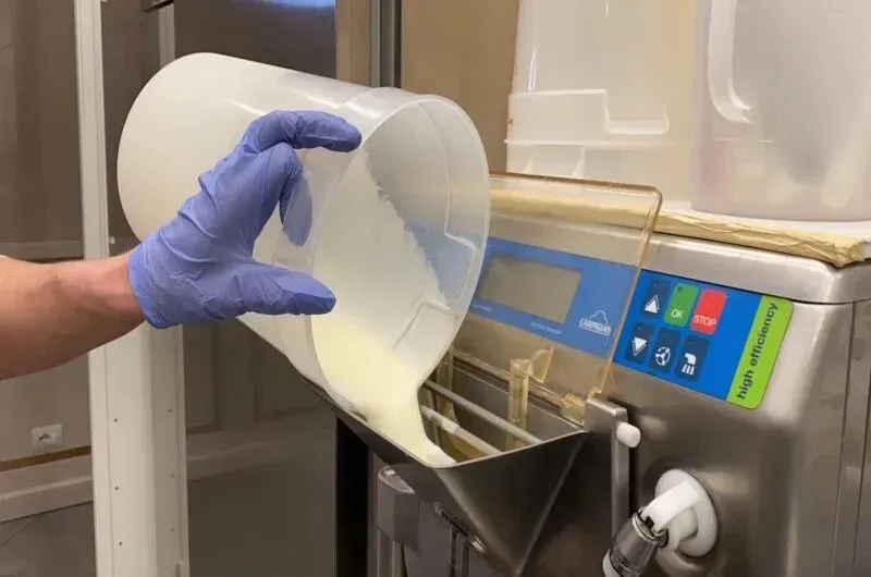 A participant pouring prepared gelato base into a professional gelato-making machine during a hands-on masterclass, demonstrating the churning and freezing process of authentic Italian gelato.