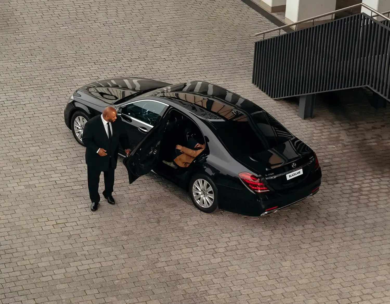 Aerial view of professional chauffeur opening door of luxury black Mercedes sedan for client during premium Rome tour service