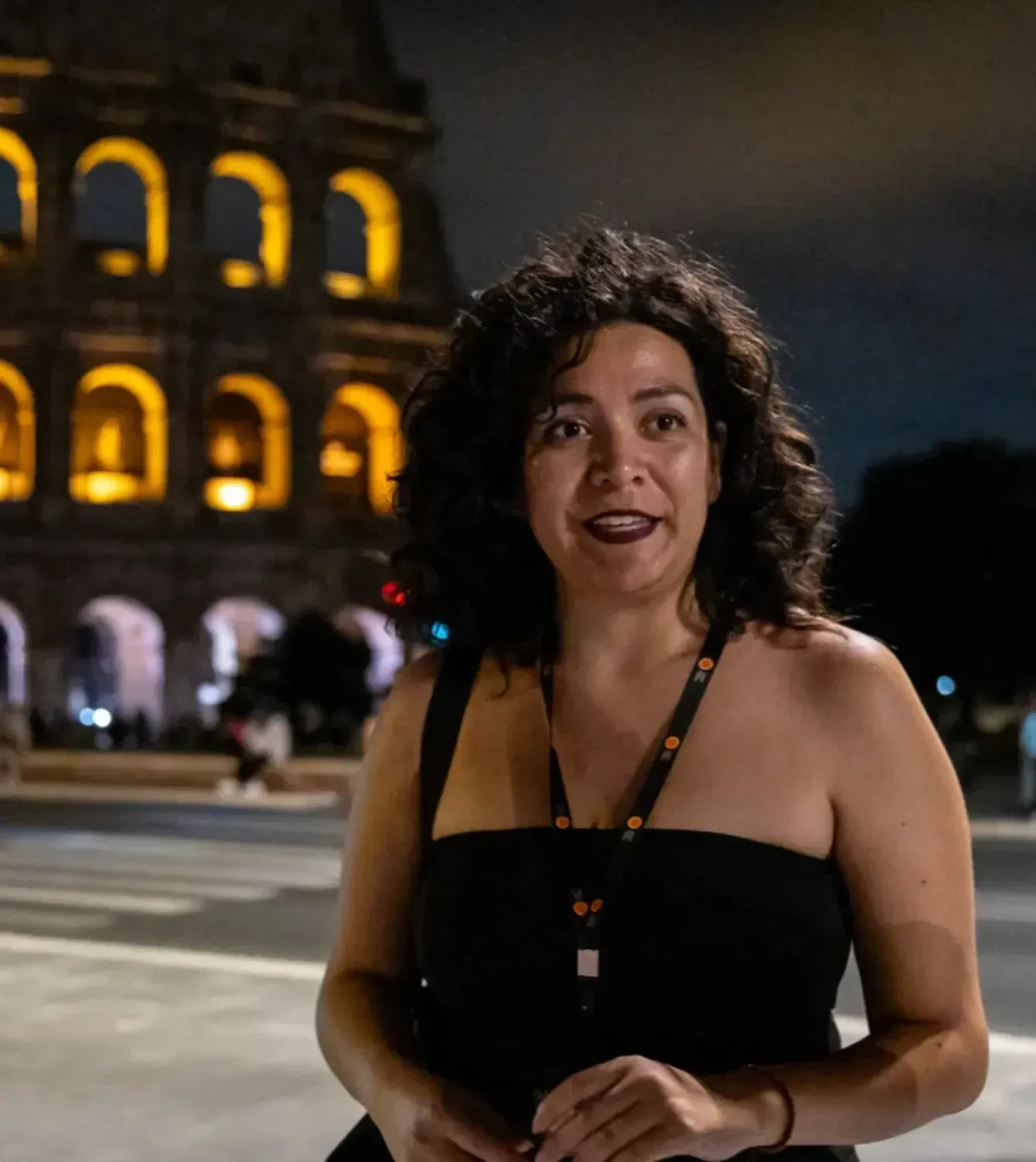Female tour guide smiling at the camera with the illuminated Colosseum and classical architecture in the background