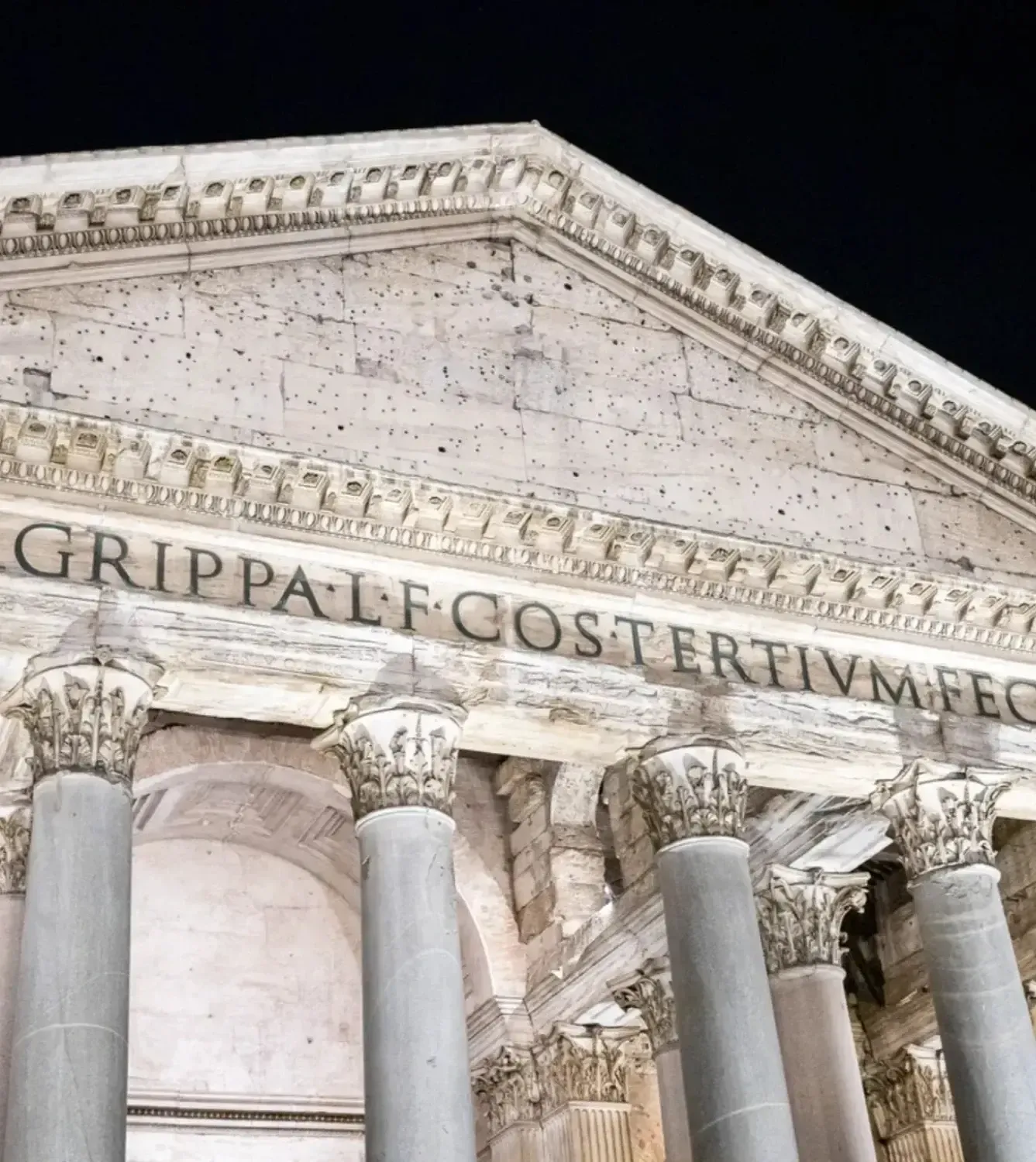 Close-up of the Pantheon's illuminated classical facade with ornate Corinthian capitals and Latin inscription at night