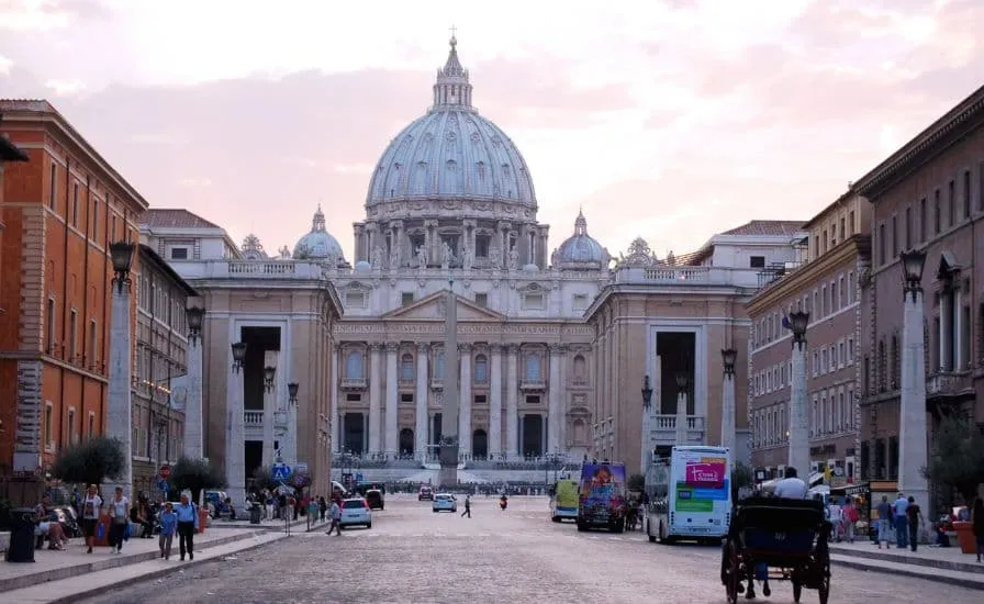 St. Peter's Basilica in Vatican with iconic dome, tourists in the square, and pink hour lighting during daytime