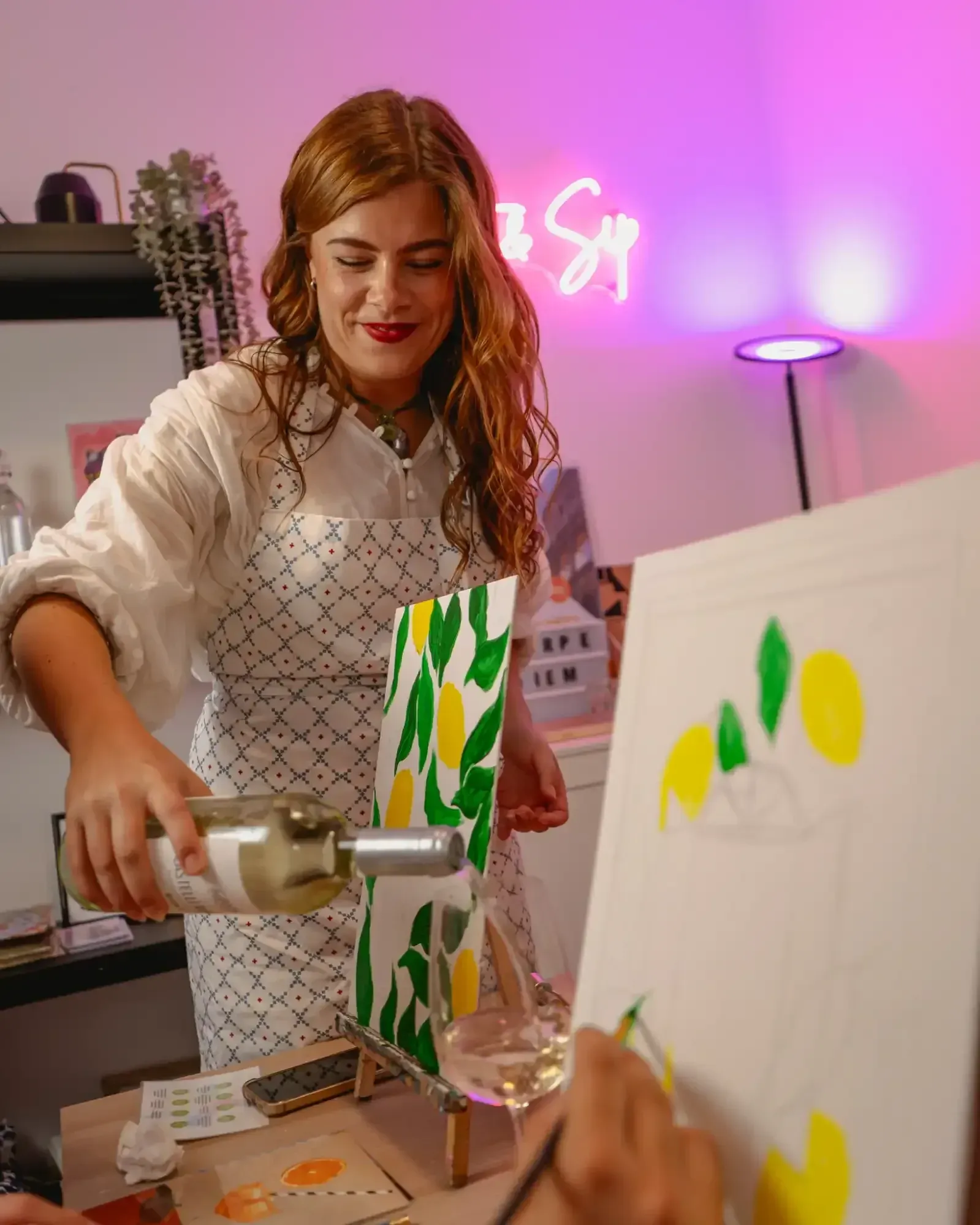 Woman painting on canvas during private tipsy art class in Rome with pink neon studio lighting