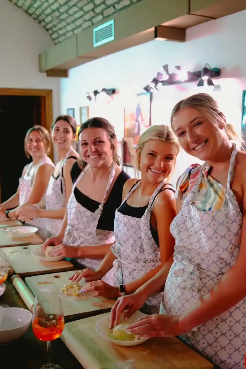 Group of five happy women in Rome with Chef aprons standing together making fresh pasta dough during the cooking class