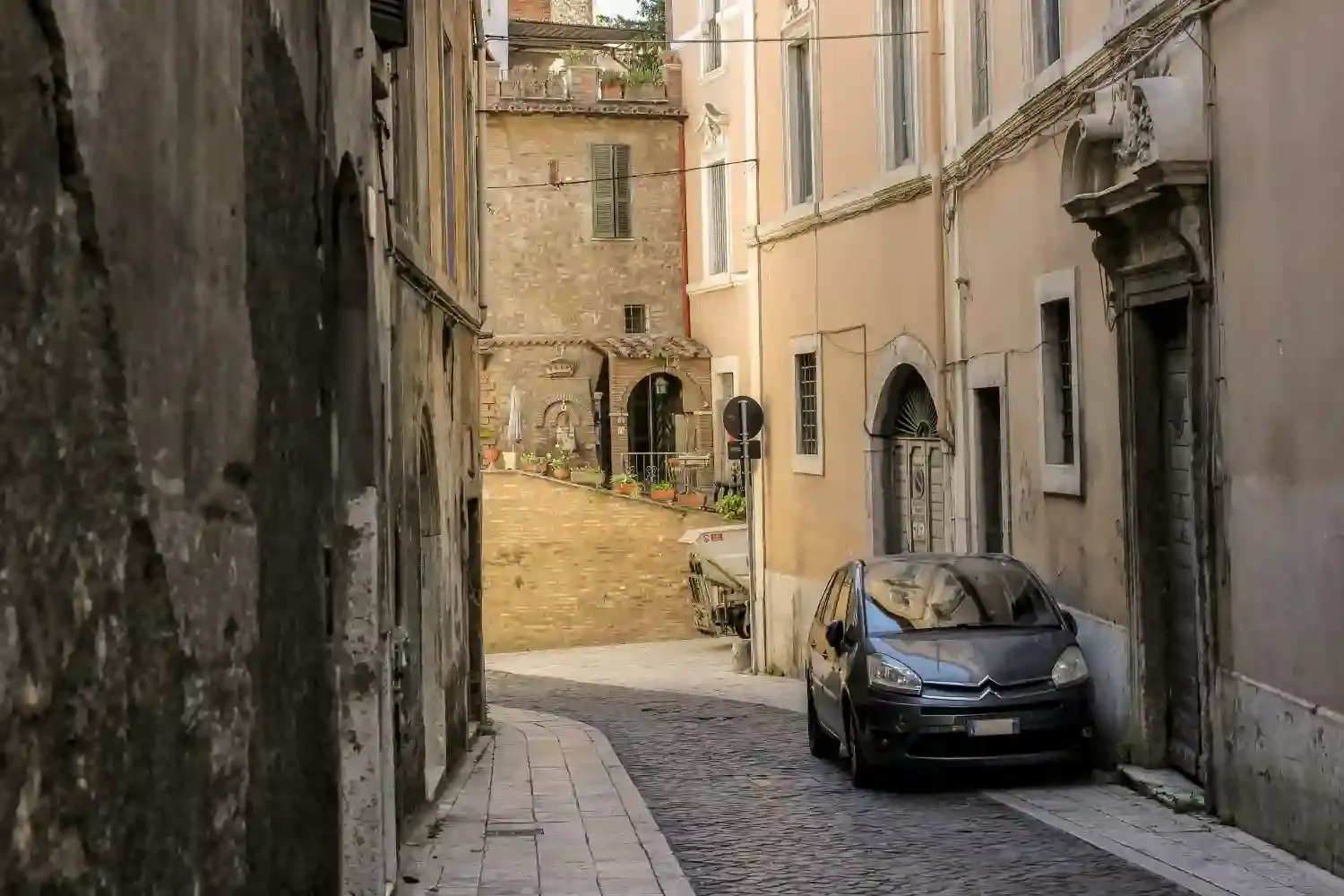 Narrow cobblestone street in historic Tivoli town with traditional Italian buildings and parked car