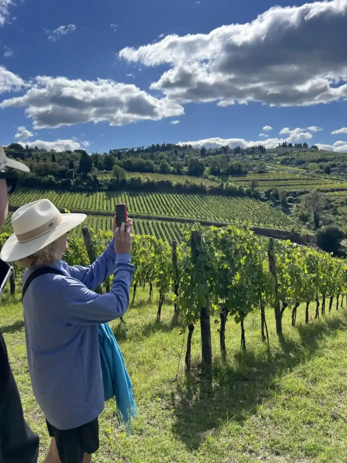 A woman on a wine tour taking a photo of the beautiful, rolling vineyards in Tuscany with her phone.