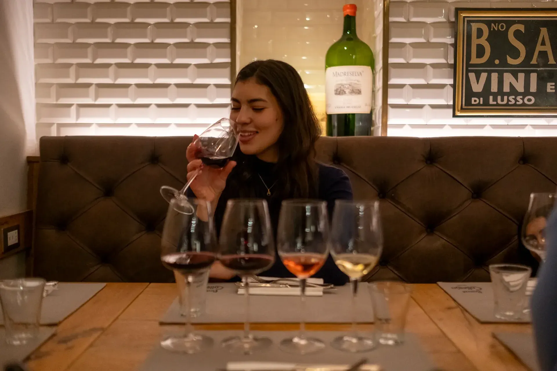 A woman smelling and tasting red wine from a flight of four different glasses.